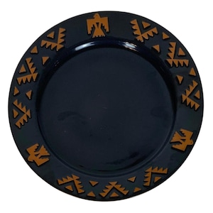May include: A dark blue plate with a decorative border featuring geometric and bird-like shapes in a warm brown color. The plate has a glossy finish and a simple, elegant design, suitable for serving food.