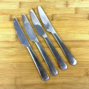Op de afbeelding: Vier zilveren dinermessen op een houten oppervlak.