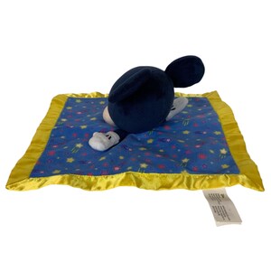 May include: A plush security blanket featuring a dark blue Mickey Mouse head with rounded ears attached to a square blue fabric center. The fabric is patterned with small yellow stars and pink shapes, finished with a bright yellow satin border.