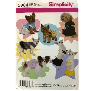 May include: Simplicity pattern 2904 featuring various dog outfits. The pattern includes designs for dresses, shirts, and other apparel. The image shows several small dogs modeling the outfits, with the text "#1 Dog" on one shirt.