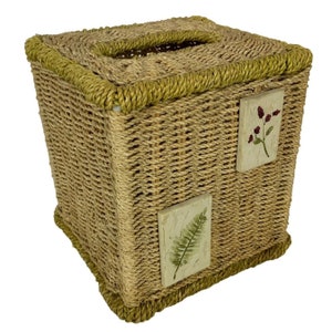 May include: A woven tissue box cover with a green rope trim and floral designs. The cover is made of natural materials and has a rustic look.