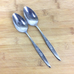 Puede incluir: Dos cucharas de plata con diseños florales sobre una superficie de madera.