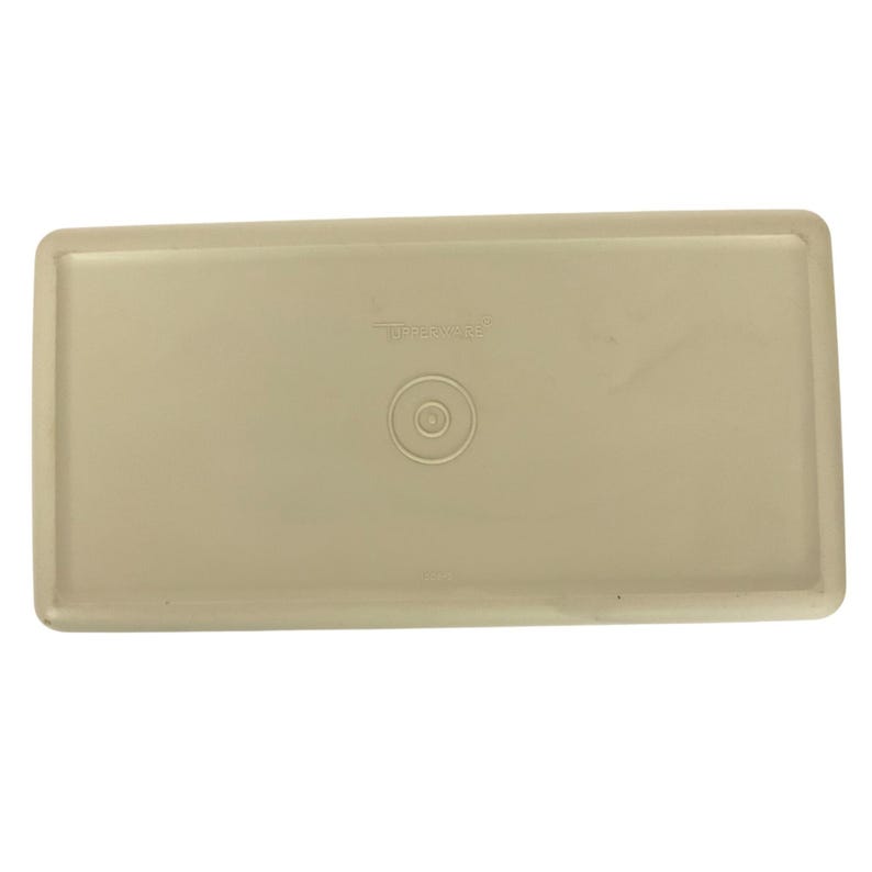 Pode incluir: Uma tampa Tupperware retangular bege. A tampa tem uma borda ligeiramente elevada e uma reentr&acirc;ncia circular no centro. O logotipo da Tupperware &eacute; vis&iacute;vel na parte superior. A tampa &eacute; feita de um material pl&aacute;stico dur&aacute;vel.
