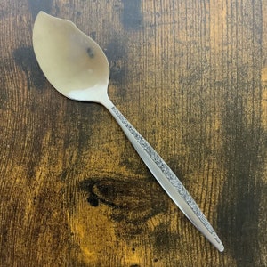 Puede incluir: Una cuchara de plata con un diseño floral en el mango. La cuchara tiene un cuenco redondeado y un mango largo y delgado.