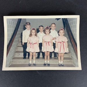 Impresión fotográfica a color de un grupo de niños con vestidos rosas y camisas blancas, 1965