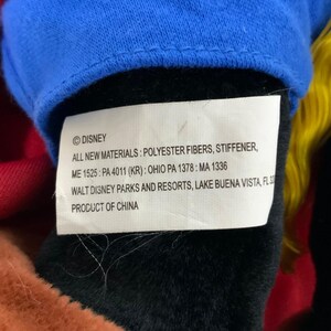 Peut inclure: Une &eacute;tiquette blanche avec du texte noir qui indique "&copy;DISNEY ALL NEW MATERIALS: POLYESTER FIBERS, STIFFENER, ME 1525: PA 4011 (KR): OHIO PA 1378: MA 1336 WALT DISNEY PARKS AND RESORTS, LAKE BUENA VISTA, FL 32 PRODUCT OF CHINA"