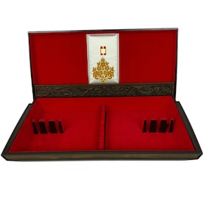 May include: Open wooden box with a red velvet interior. The box has a decorative gold and white panel on the inside of the lid. The box has slots and dividers for storage. The exterior is a dark brown color.