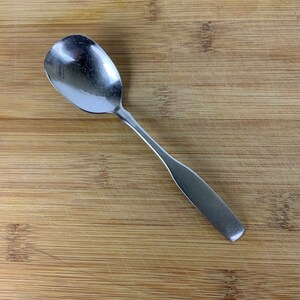 Op de afbeelding: Een zilveren lepel met een ronde kom en een lange, slanke steel. De lepel ligt op een houten oppervlak.