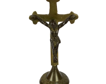 May include: A gold-toned metal crucifix with a dark-toned metal figure of Jesus Christ. The crucifix has a decorative base with a floral design.