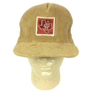 May include: A tan corduroy trucker hat with a red and white patch featuring a stylized outline of the state of Texas and the letters "UT" inside.