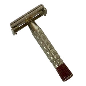May include: A vintage safety razor with a silver head and handle. The handle features a textured, checkered pattern and a dark red, ribbed base. The razor is designed for shaving and personal grooming.