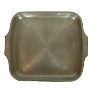 Peut inclure: Un plateau de service carré en métal avec une finition argentée brossée. Le plateau présente des coins arrondis et deux poignées latérales intégrées, chacune décorée de quatre lignes horizontales gravées. La surface a une texture polie.