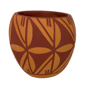 May include: A rounded terracotta pot featuring a matte finish with a repeating geometric pattern in dark brown and light orange. The design consists of stylized petal shapes and triangular motifs arranged in a symmetrical layout around the exterior.