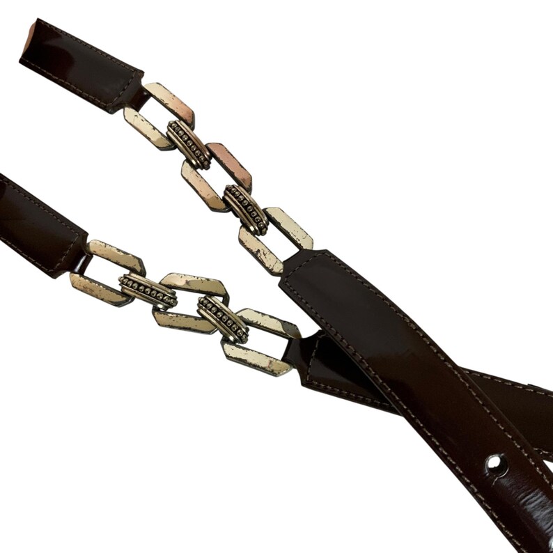 May include: A brown belt with a chain-link design. The belt features a glossy, dark brown leather strap and silver-toned metal chain links. The belt is designed with multiple holes for adjustment.