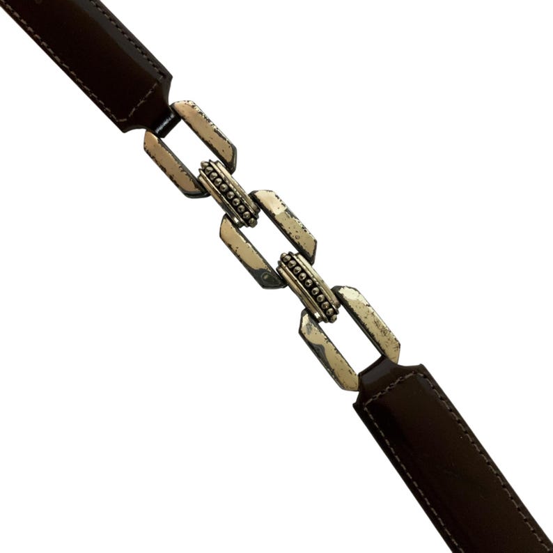 May include: A brown leather belt with a silver chain link design. The belt has a rectangular buckle and a series of interconnected links. The leather is a dark brown color, and the metal has a distressed finish.