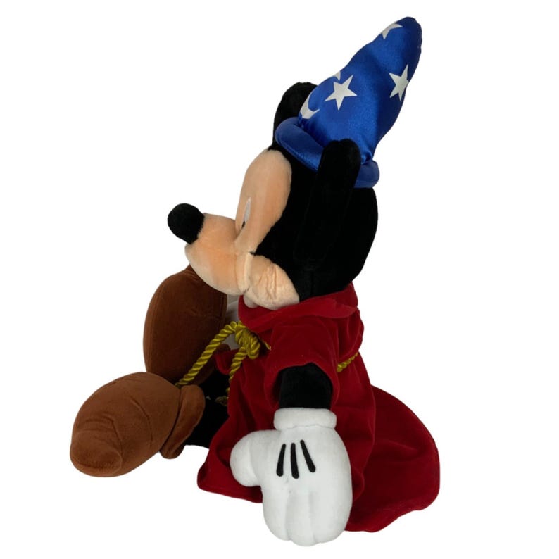 Peut inclure: Un Mickey Mouse en peluche habill&eacute; en sorcier. Il porte un chapeau bleu avec des &eacute;toiles blanches et une robe rouge. Il a un sac brun dans sa main.