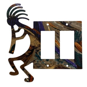 Op de afbeelding: Een dubbele lichtschakelaarplaat met een uitgesneden silhouet van een fluitspelende figuur aan de linkerkant. Het oppervlak heeft een veelkleurig abstract patroon met streken van bruin, paars, oranje en groenblauw over de hele rechthoekige plaat.