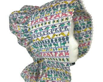Puede incluir: Un gorro blanco con un borde rizado y un estampado colorido de pájaros, flores y animales. El estampado presenta colores rosa, amarillo, azul y verde.