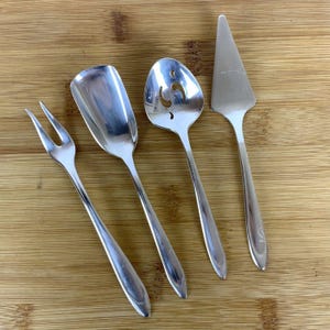 May include: Four silver-plated serving utensils: a fork, a small spoon with a decorative cut-out design, a small serving spoon, and a cake server.
