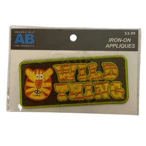 Könnte beinhalten: Ein rechteckiger Aufbügler auf einer Präsentationskarte. Der Aufnäher hat einen braunen Hintergrund mit einem gelb-orangen Tigergesicht auf der linken Seite und dem Text WILD THING in gelben und orangen Blockbuchstaben rechts, umrandet in Limettengrün.