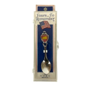 May include: A silver souvenir spoon with a red and yellow design featuring the words "Golden Gate Bridge" and "San Francisco, CA". The spoon is packaged in a clear plastic box with a white label that reads "Yours...To Remember" and a small American flag. The label also includes the text "F.O.R.T. Made in U.S.A."