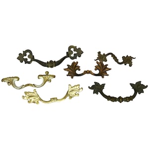 May include: Five ornate metal drawer pulls with a variety of designs. The pulls are in shades of gold, bronze, and copper.