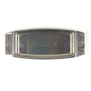 Puede incluir: Una bandeja rectangular de plata con bordes decorativos. La bandeja está hecha de acero inoxidable y tiene una superficie lisa y pulida.