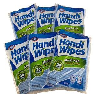 Op de afbeelding: Zes verpakkingen Clorox Handi Wipes multifunctionele herbruikbare doekjes gerangschikt in een groep. Elke doorzichtige plastic verpakking heeft een blauwe en groene branding met de tekst Handi Wipes, Multi-Use Reusable Cloths en een Rinse & 20 Times Reuse logo.
