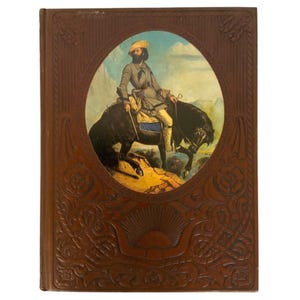 May include: A vintage brown leather-bound book with an oval illustration of a man on horseback. The cover features embossed floral and sunburst designs. The illustration depicts a man in period clothing riding a black horse.