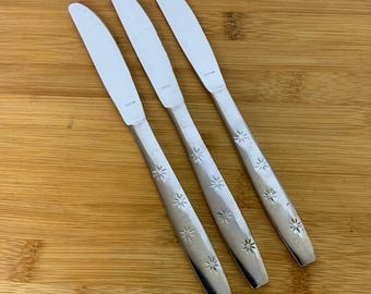 May include: Three silver dinner knives with star-shaped designs on the handles.
