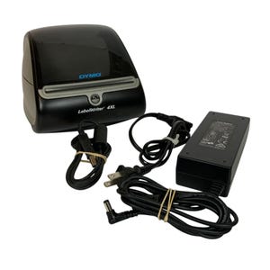 May include: A black Dymo LabelWriter 4XL thermal label printer with a glossy top cover, a grey paper feed slot, and a power adapter with a black cord. The printer features the Dymo logo in blue and the text LabelWriter 4XL printed on the front panel.