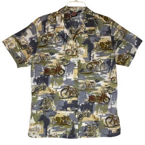 Può includere: Camicia a maniche corte con stampa di motociclette nei toni del grigio, verde e beige. La camicia ha un colletto classico e una chiusura con bottoni. I disegni delle motociclette sono in vari stili.