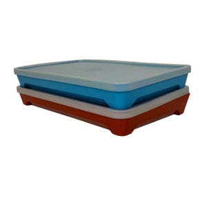 May include: Two rectangular food storage containers. The bottom container is red with a white rim, and the top container is blue with a white rim. Both containers have matching light blue lids.