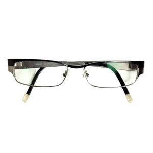 Puede incluir: Gafas negras y plateadas con lentes rectangulares. Las monturas tienen un diseño elegante y moderno con la parte superior negra e inferior plateada. Las patillas son negras con puntas blancas. La marca "DKNY" es visible.