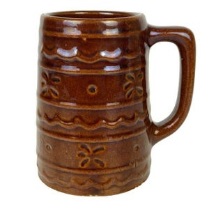 Könnte beinhalten: Eine braune Keramiktasse mit Henkel. Die Tasse hat ein wellenförmiges Design und ein Blumenmuster.