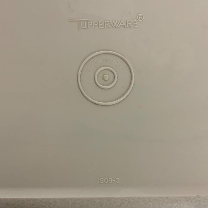 Pode incluir: Uma tampa de recipiente Tupperware cinza claro em close-up. A tampa apresenta o logotipo da Tupperware, um selo circular "Made in U.S.A." e o n&uacute;mero "1508-3".