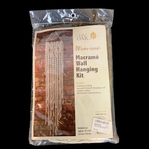 May include: A packaged macramé wall hanging kit. The kit includes cotton cording, a natural branch hanging rod, and copper tubes. The finished size is approximately 10" x 48". The packaging features a brick wall background and the words "Make-ramé" and "Macramé Wall Hanging Kit".