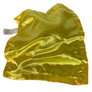 May include: A square, bright yellow satin security blanket featuring a smooth, shiny finish and a wide, stitched border. A white rectangular fabric tag with black printed text is attached to the upper left corner of the yellow fabric.