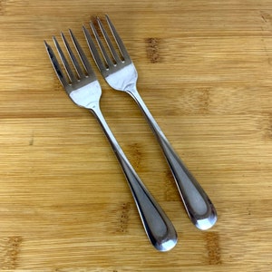 May include: Two silver forks on a wooden surface.