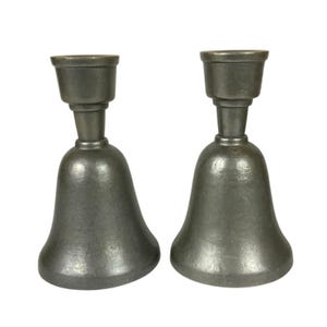 Puede incluir: Un par de candelabros de metal gris oscuro a juego con una base en forma de campana y una sección superior cilíndrica. Cada candelabro presenta un acabado mate liso y una base ancha y acampanada que se estrecha hacia un cuello fino.