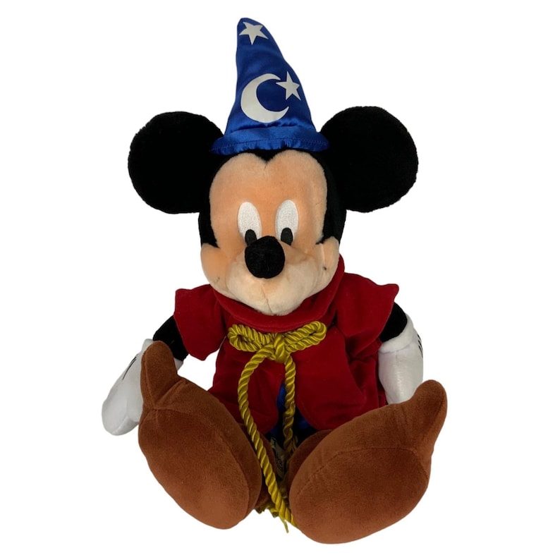 Peut inclure: Un Mickey Mouse en peluche portant un chapeau de magicien bleu avec des &eacute;toiles et une lune croissante. Il porte une robe rouge avec une corde dor&eacute;e attach&eacute;e autour de sa taille. Il est assis les jambes crois&eacute;es.