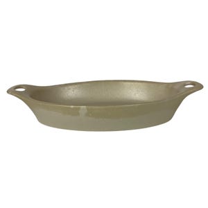 Puede incluir: Una fuente de horno ovalada de cerámica en una paleta de colores apagados y terrosos. La fuente tiene una superficie ligeramente texturizada y un color beige claro que pasa a un tono verde oliva más oscuro cerca de la base. Cuenta con un asa con un agujero en cada extremo.