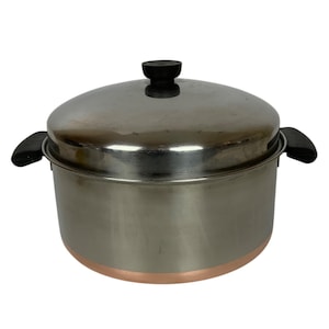 Puede incluir: Olla de cocina de acero inoxidable con base de color cobre y tapa a juego. La olla tiene asas negras y un pomo negro en la tapa. Diseñada para cocinar y preparar alimentos.