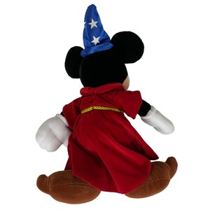 Peut inclure: Un Mickey Mouse en peluche habill&eacute; en sorcier. Il porte un chapeau bleu avec des &eacute;toiles blanches, une robe rouge avec une ceinture dor&eacute;e et des chaussures marrons.