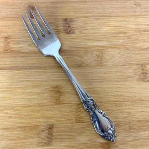 May include: A silver fork with an ornate handle. The handle has a floral design.