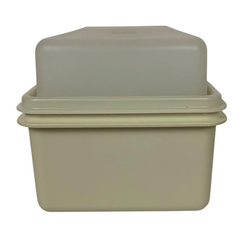 Pode incluir: Um recipiente retangular vintage para armazenamento de alimentos com tampa. O recipiente e a tampa s&atilde;o de cor bege claro. A tampa fica em cima do recipiente, e o recipiente tem uma borda ligeiramente elevada.