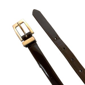 May include: A dark brown leather belt with a silver-colored buckle. The belt is glossy and has a rectangular buckle. The belt is unbuckled and the strap is separated from the buckle.