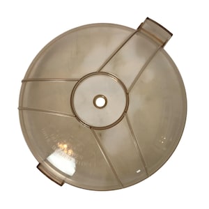 Puede incluir: Una tapa circular transparente con un agujero central y soportes radiales. La tapa tiene un asa y el texto "DO NOT OPEN UNTIL BLADES STOP".