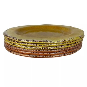 May include: A stack of four yellow and brown ceramic dinner plates with a speckled glaze.