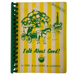 May include: A vintage cookbook with a green spiral binding. The cover has a yellow and white striped pattern, a green illustration of a horse-drawn carriage, and the text "Talk About Good!". The book is titled "Le Livre de la Cuisine de Lafayette".